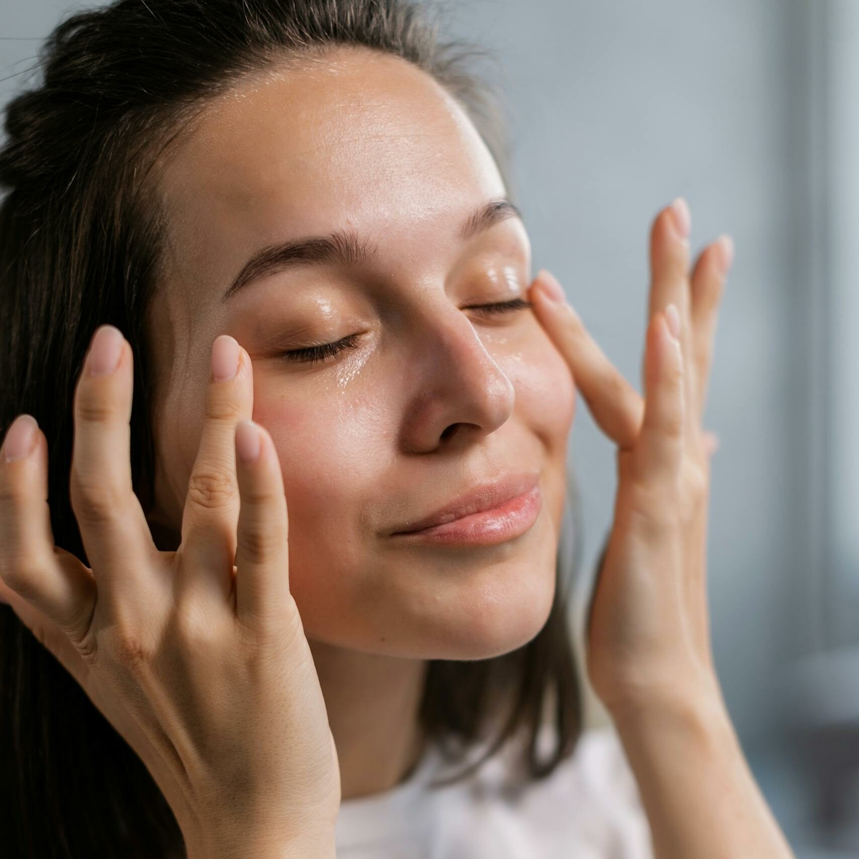 Young woman applying skincare cream with a smile, highlighting self-care and beauty routines.