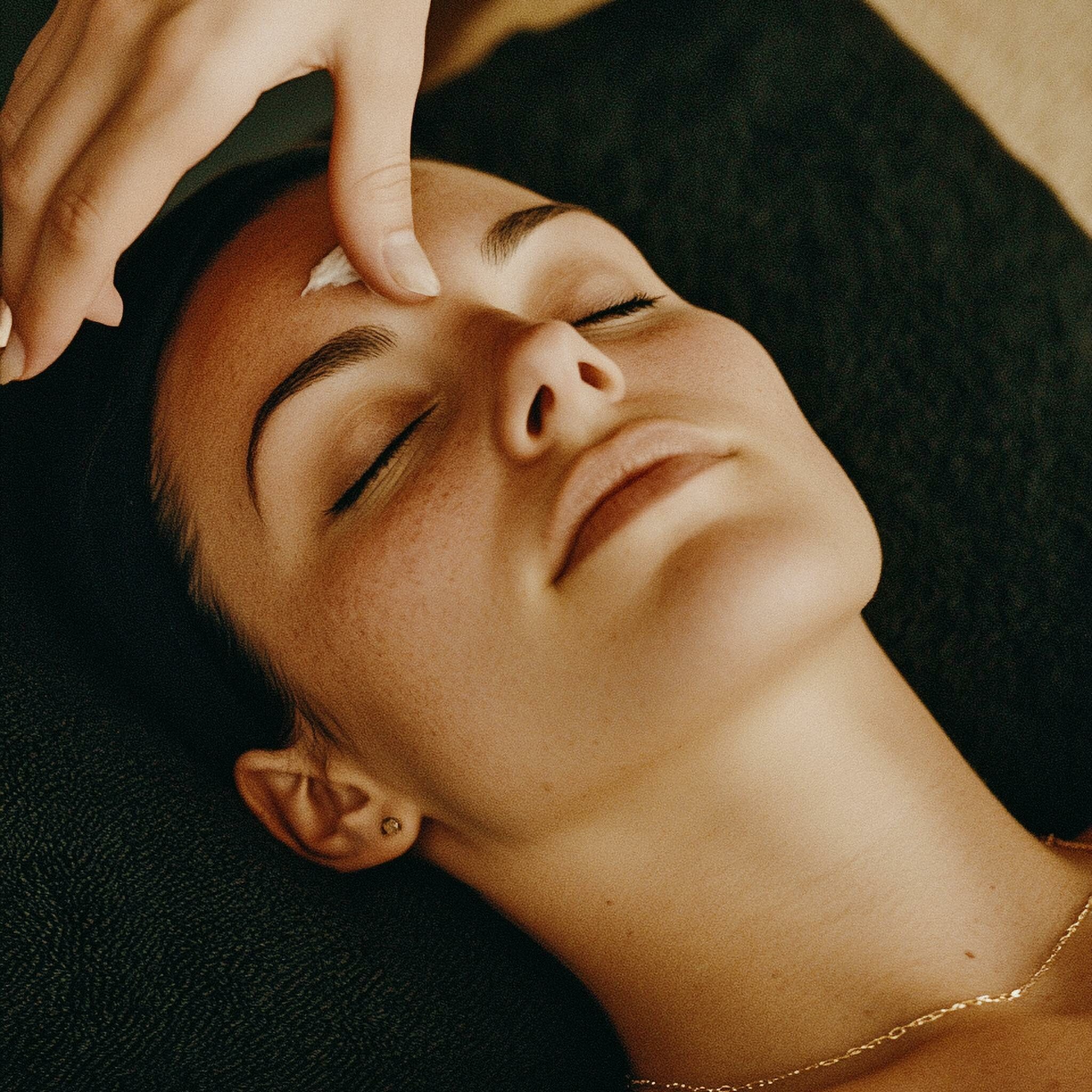 Peaceful woman enjoying a rejuvenating facial treatment with warm ambiance.